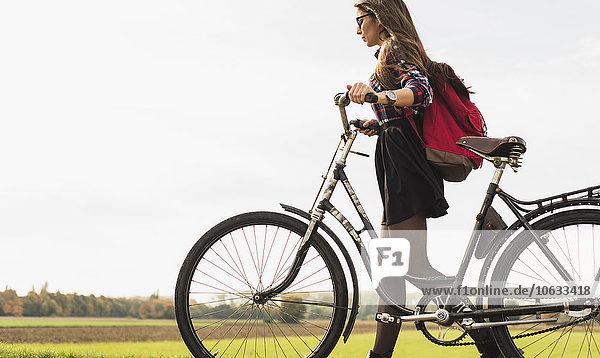 Junge Frau schiebt ihr Fahrrad in ländlicher Landschaft