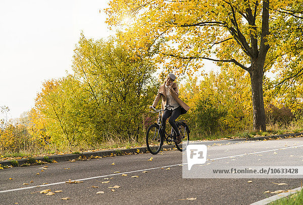 Junge Frau auf dem Handy beim Fahrradfahren in der Herbstlandschaft