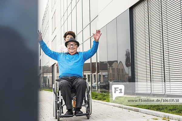 Seniorin mit jubelndem Ehemann im Rollstuhl auf dem Bürgersteig
