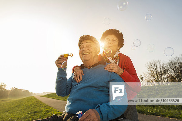 Senior woman with husband in wheelchair blowing soap bubbles