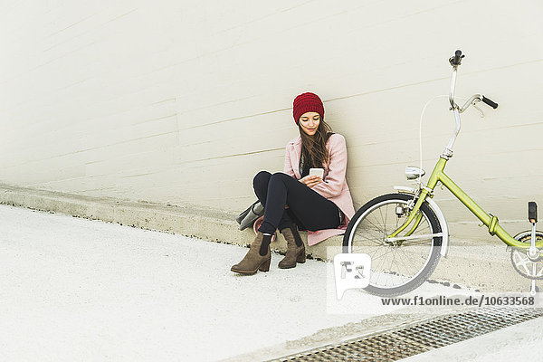 Junge Frau sitzt neben dem Fahrrad und schaut aufs Handy.