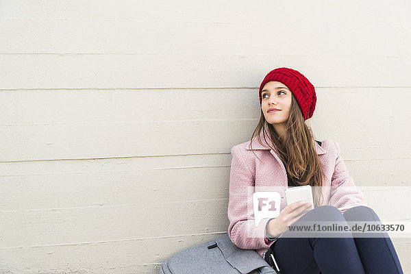 Junge Frau sitzt an der Betonwand und hält Handy