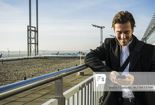 Germany  Frankfurt  Young businessman at the airport using smartphone