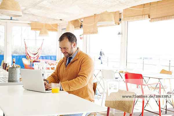 Spain  Barcelona  smiling businessman sitting at seaside cafe using laptop
