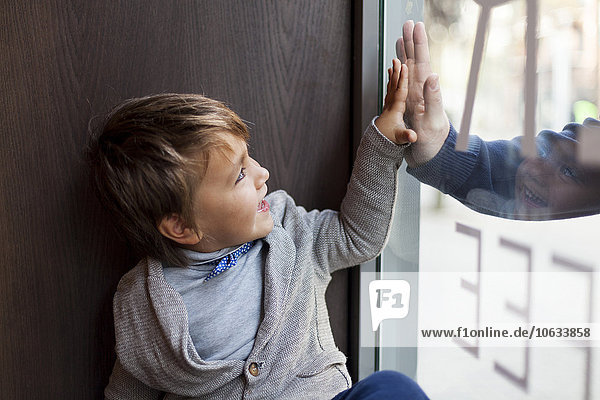 Porträt eines kleinen Jungen  der durchs Fenster auf seinen Vater schaut  der draußen steht.