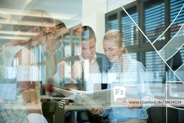 Erfolgreiches Business-Team hinter Glaswand im Büro mit Blick auf Ordner