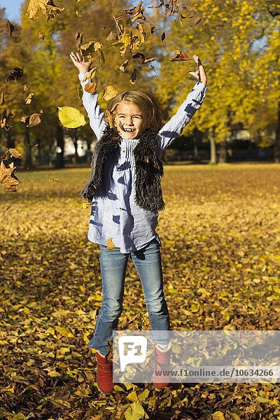 Happy little girl throwing autumn leaves while jumping in the air