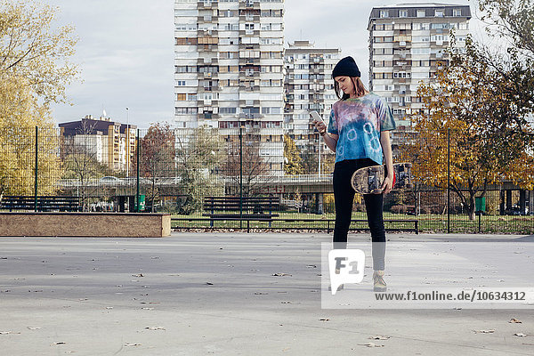 Young woman with skateboard looking at cell phone