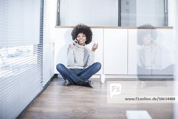 Woman sitting on the floor in office using cell phone