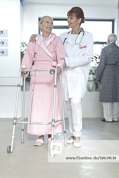 Doctor leading elderly patient with walking frame on hospital floor