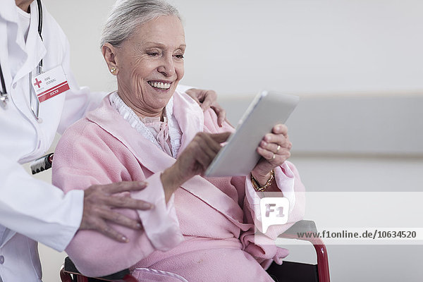 Lächelnder älterer Patient im Rollstuhl mit digitalem Tablett