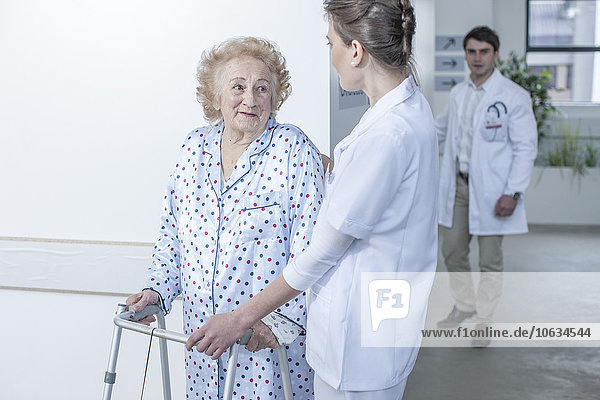 Nurse leading elderly patient with walking frame on hospital floor