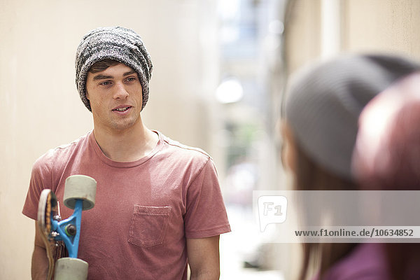 Young man with skateboard in a passageway talking to friends