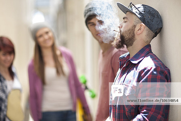Junger Mann raucht eine Zigarette mit Freunden im Hintergrund