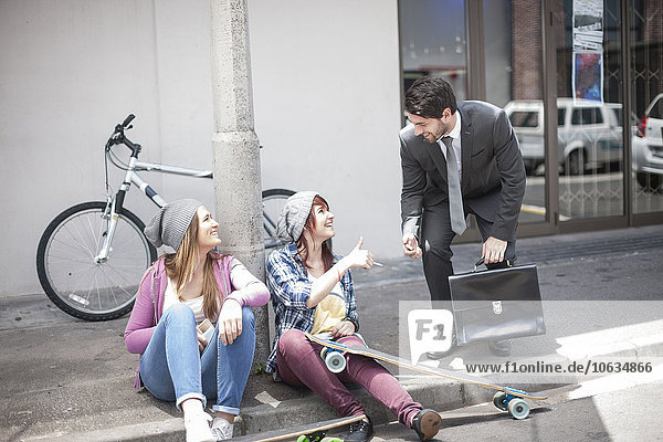 Businessman giving a lighter to two female friends on city street