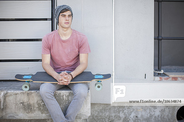 Junger Mann mit Skateboard im Freien sitzend