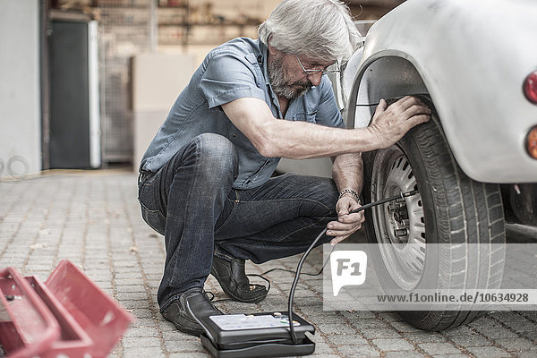 Senior man at car measuring tire pressure