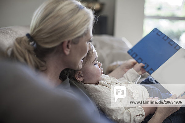 Mother and baby girl at home looking at book