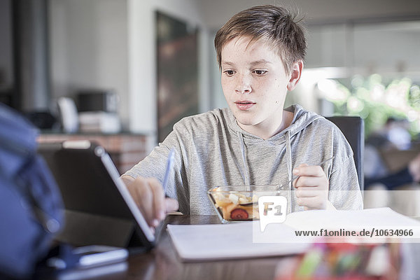 Boy at home eating fruit salad and using digital tablet