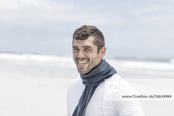 Porträt eines lachenden Mannes mit blauem Schal am Strand
