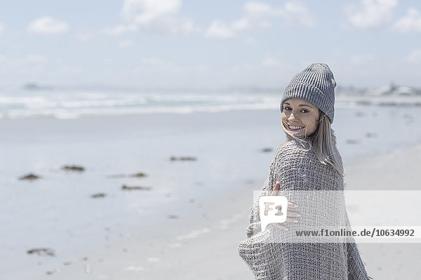 Porträt einer lächelnden Frau in Mütze und Wickeltuch am Strand