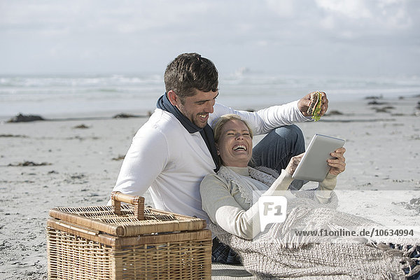 Couple with digital tablet having picnic on a beach