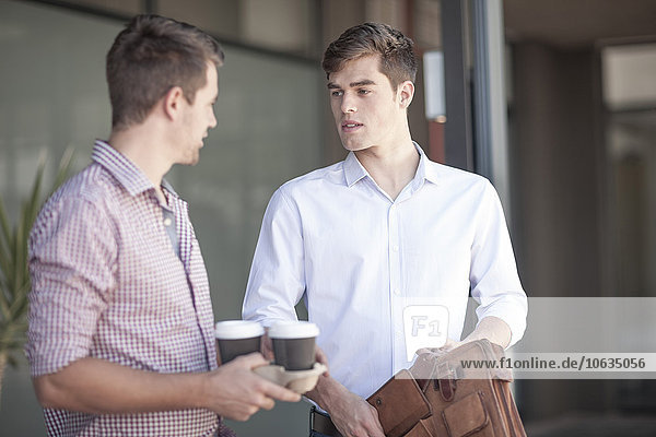 Colleagues talking in the street  holding coffee cups