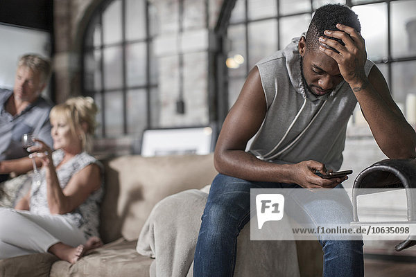 Young man sitting on couch with cellphone looking worried