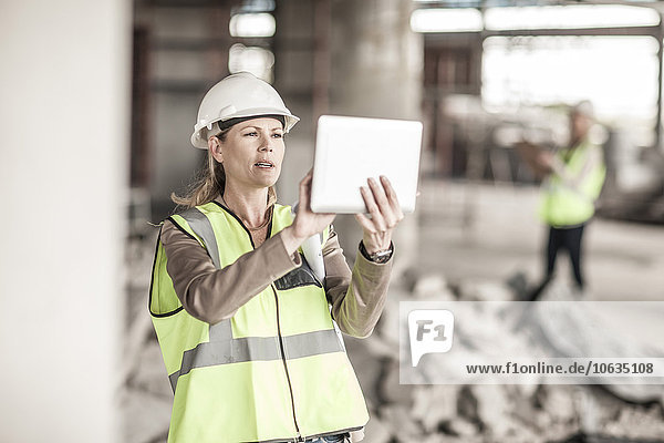 Frau in Arbeitsschutzbekleidung mit digitalem Tablett auf der Baustelle