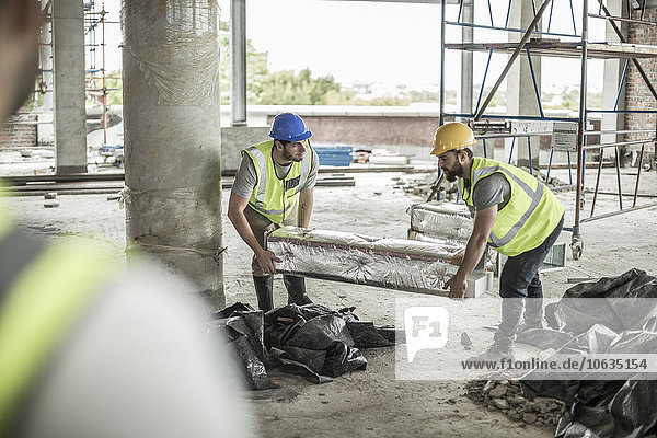 Zwei Bauarbeiter  die Gegenstände auf der Baustelle befördern