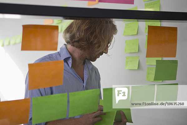 Man putting adhesive notes on glass wall in office