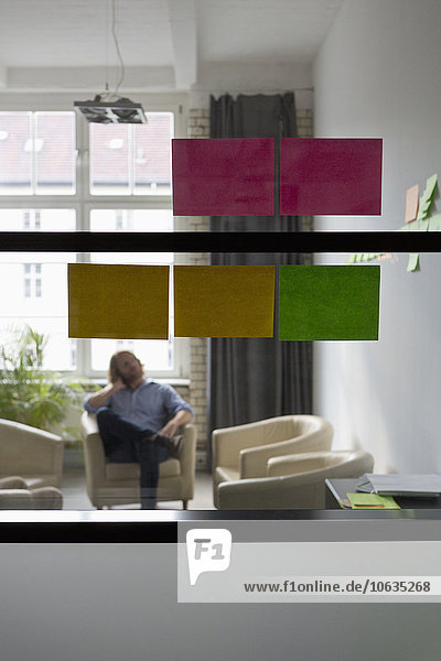 Adhesive notes on glass wall  man sitting on sofa in background
