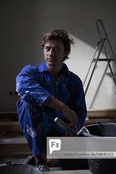 Mann in Arbeitskleidung sitzend mit Farbeimer  Portrait