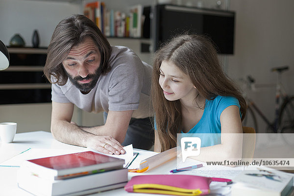 Father assisting daughter in doing homework at table