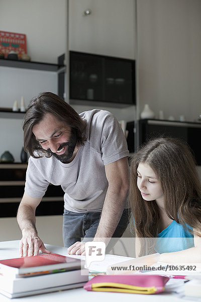 Lächelnder Vater hilft der Tochter bei den Hausaufgaben am Tisch