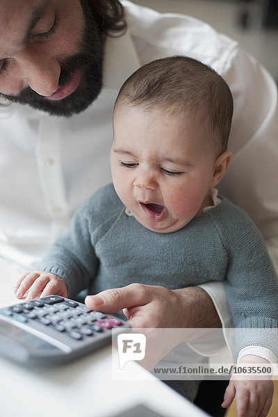 Cute baby girl yawning with father using calculator at home