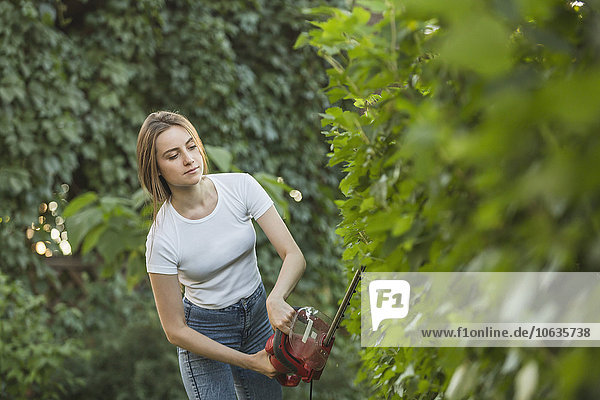 Young woman cutting plants with hedge clipper at yard