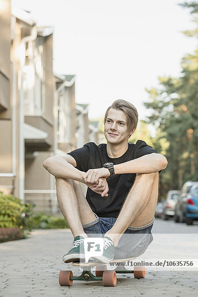 Nachdenklicher junger Mann sitzt auf einem Skateboard im Freien.