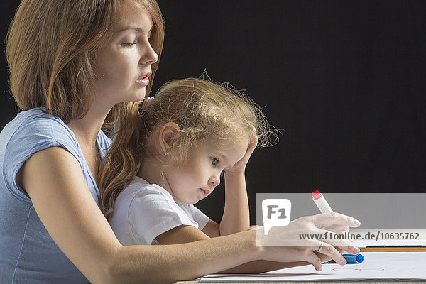 Seitenansicht der Mutter assistierendes Mädchen beim Zeichnen vor schwarzem Hintergrund