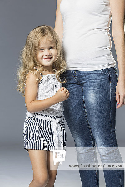 Portrait of happy girl standing with mother against gray background