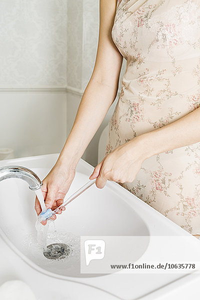 Mittelteil der Frau  die die Zahnbürste am Waschbecken wäscht.