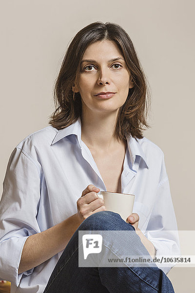 Portrait of confident woman holding coffee mug against white background