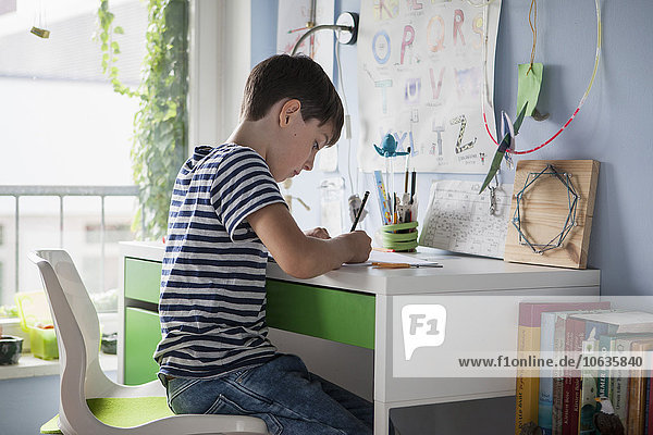 Seitenansicht des Jungen bei den Hausaufgaben am Tisch im Haus