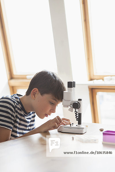 Neugieriger Junge mit dem Mikroskop auf dem Tisch zu Hause