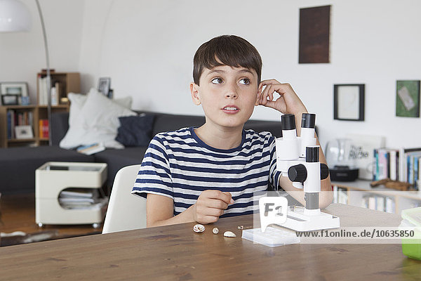 Nachdenklicher Junge mit Mikroskop im Wohnzimmer zu Hause