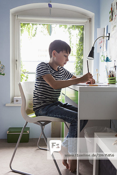 Junge macht Hausaufgaben bei Tisch im Haus