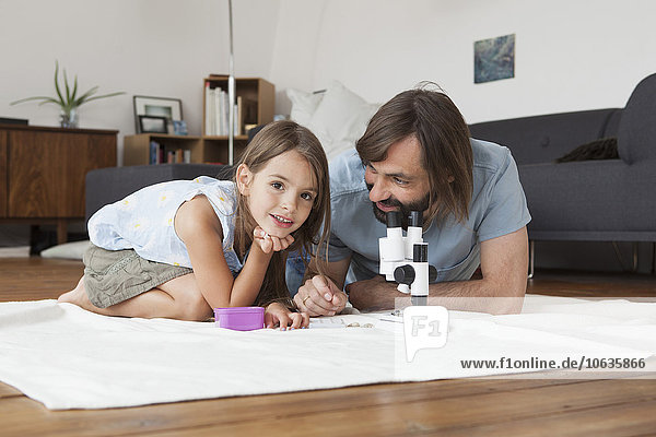 Vater und Tochter mit dem Mikroskop auf dem Teppich zu Hause