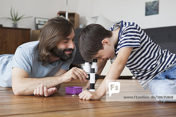 Father and son using microscope on hardwood floor