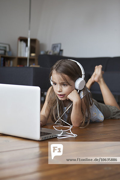 Cute girl listening music while using laptop on hardwood floor at home
