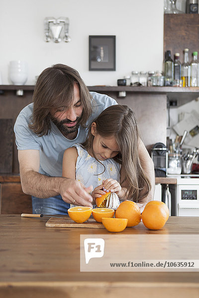 Vater hilft der Tochter beim Auspressen von Orangen aus dem Entsafter auf dem Tisch zu Hause.